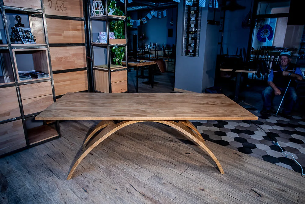 Tavolo "Old Bridge" con struttura robusta e design sofisticato Tavolo rettangolare in legno chiaro con base ad arco doppio, perfettamente bilanciato per un ambiente accogliente e moderno.